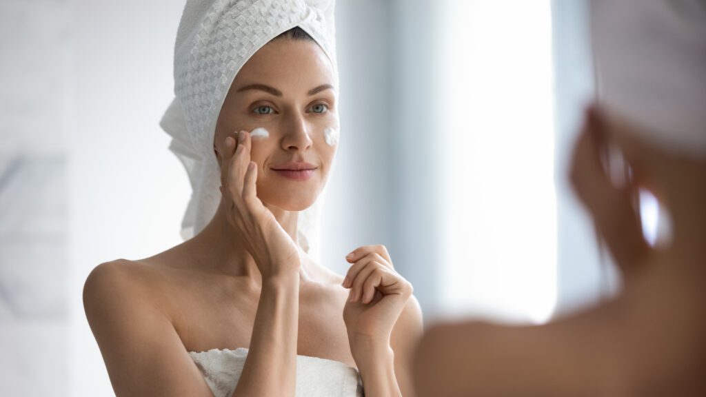 young woman in mirror applying skin care products to face